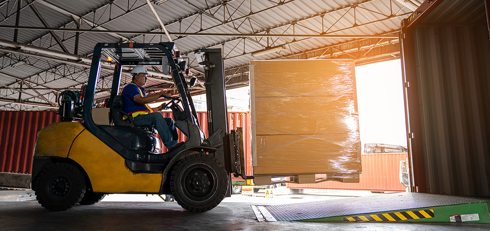 Warehouse worker driver in uniform delivery and loading pallet product by forklift.